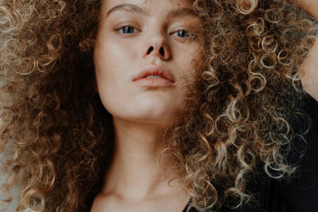 Close-up portrait of a young woman with natural curly hair and minimal makeup.